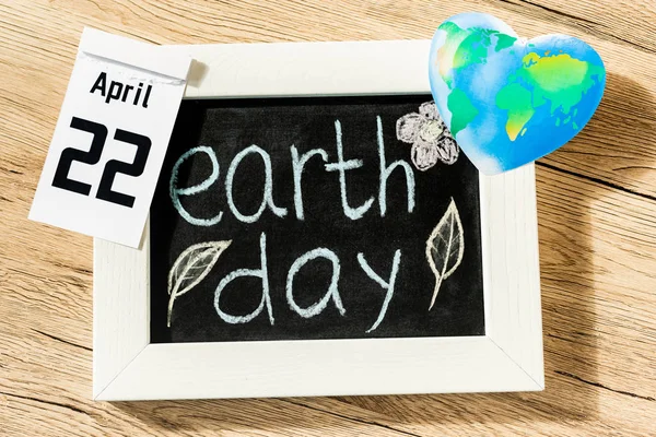 Top view of board with earth day lettering, globe and calendar with 22 april inscription on wooden background — Stock Photo