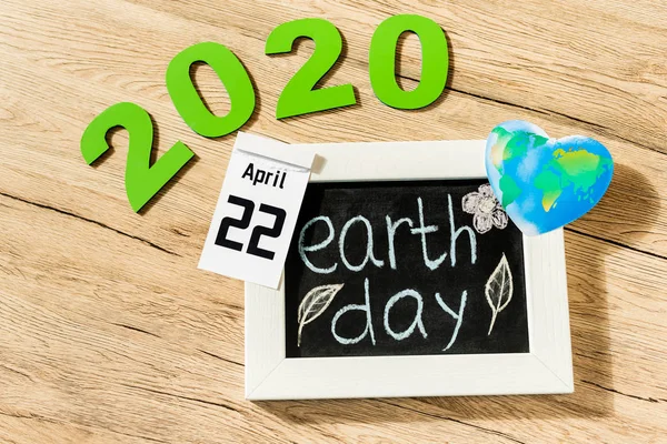 High angle view of board with earth day lettering, calendar with 22 april 2020 inscription and globe on wooden background — Stock Photo