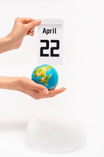 Vue recadrée du calendrier avec inscription du 22 avril et globe entre les mains d'une femme sur fond blanc, concept de réchauffement climatique — Photo de stock