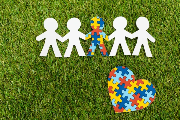 Vue du dessus de l'enfant spécial avec autisme parmi un autre et coeur de puzzle décoratif sur fond vert — Photo de stock