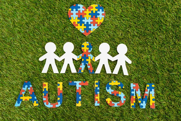 Top view of autism puzzle lettering, decorative heart and special kid among another on green — Stock Photo