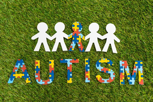 Top view of autism puzzle lettering and special kid among another on green background — Stock Photo