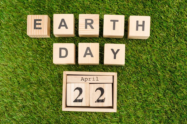 Top view of wooden cubes with earth day and 22 april lettering on green background — Stock Photo