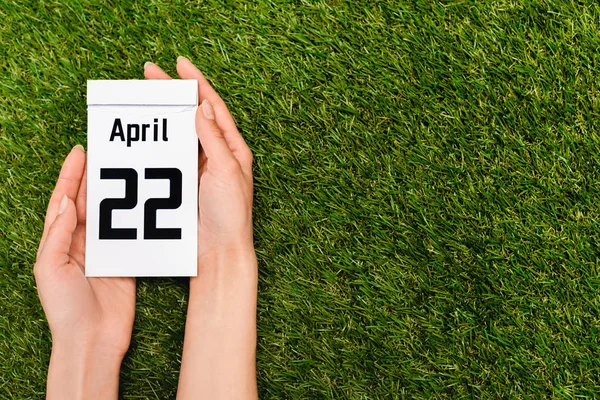 Vista cortada de calendário com 22 inscrição abril em mãos femininas em verde, conceito de dia de terra — Fotografia de Stock