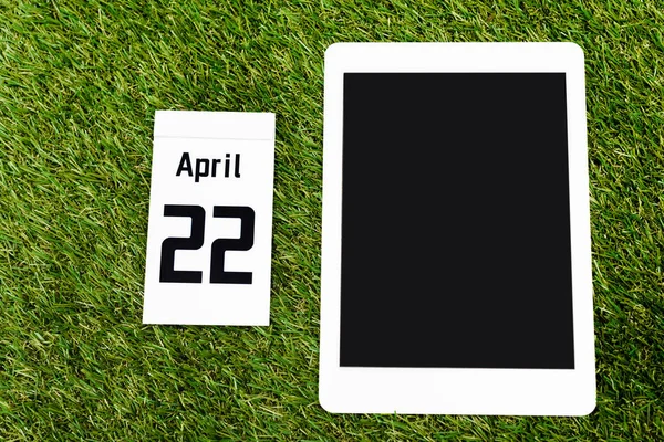 Draufsicht auf digitales Tablet und Kalender mit 22 April-Inschrift auf grünem Hintergrund, Earth Day-Konzept — Stockfoto