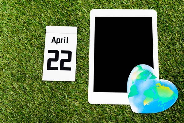 Draufsicht auf digitales Tablet, Globus und Kalender mit 22-April-Inschrift auf grünem Hintergrund, Earth Day-Konzept — Stockfoto