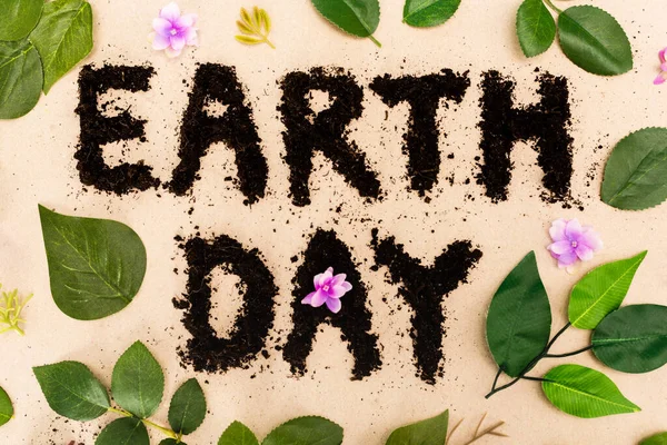 Top view of earth day lettering with leaves and buds on beige background — Stock Photo