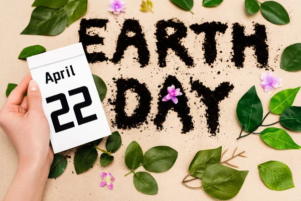 Cropped view of woman holding calendar with 22 april inscription near earth day lettering on beige — Stock Photo