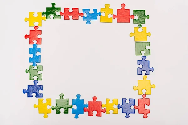 Vista superior del marco con piezas brillantes de rompecabezas aislado en blanco, concepto de autismo - foto de stock