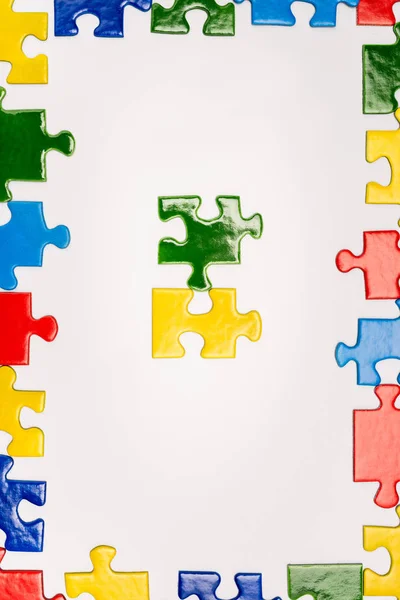 Вид зверху рамки з яскравими різнокольоровими шматочками головоломки ізольовані на білому, концепція аутизму — стокове фото