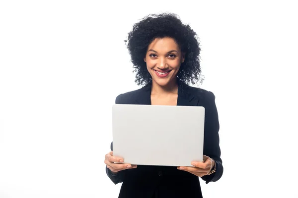 Vista frontal da empresária americana africana segurando laptop, sorrindo e olhando para a câmera isolada no branco — Fotografia de Stock