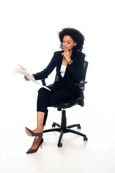 Mujer de negocios afroamericana en silla de oficina leyendo periódico sobre fondo blanco - foto de stock