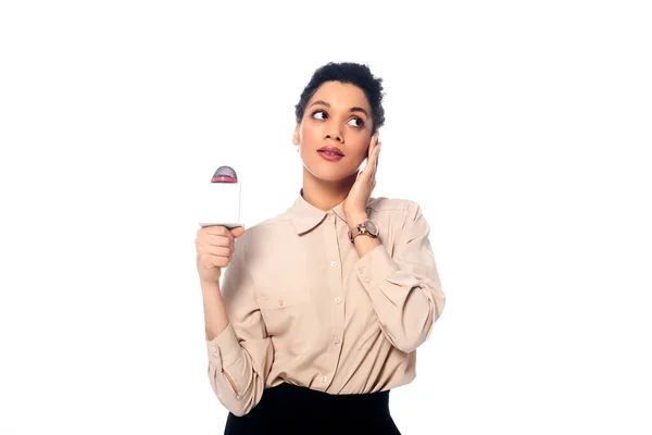 Front view of african american journalist with microphone touching face and looking away isolated on white — Stock Photo