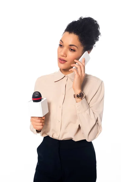 Thoughtful african american journalist with microphone talking on smartphone isolated on white — Stock Photo