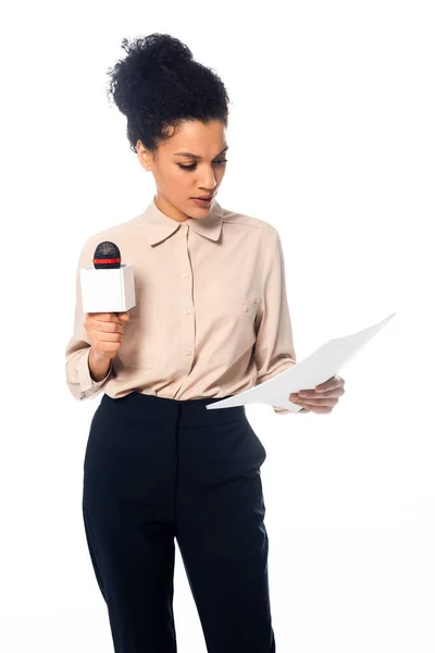 Vue de face d'un journaliste afro-américain concentré avec microphone lisant des documents isolés sur du blanc — Photo de stock