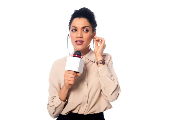 Front view of african american journalist with microphone putting headphones in ears isolated on white — Stock Photo