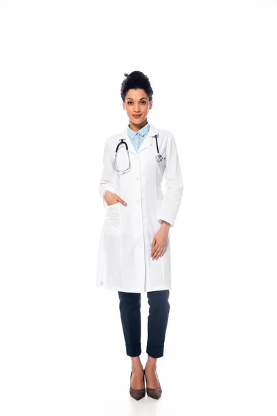 Вид спереди на африканского американского врача со стетоскопом и рукой в кармане, улыбающегося на белом фоне — стоковое фото