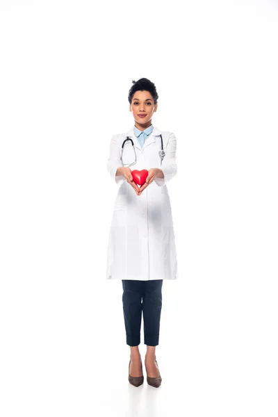 Front view of african american doctor with stethoscope smiling and presenting decorative heart on white background — Stock Photo
