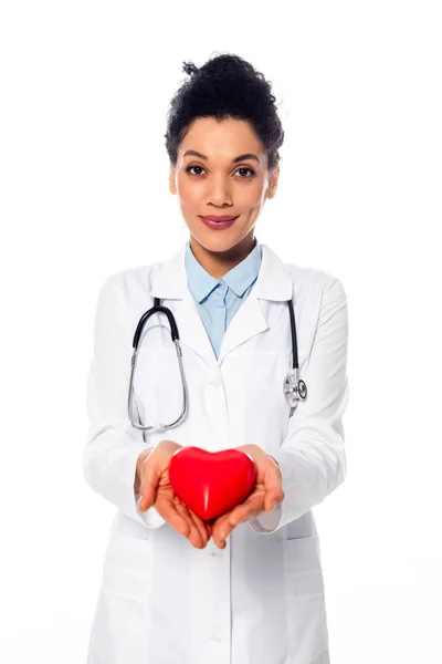 Vista frontal del médico afroamericano con estetoscopio sonriendo y mostrando el corazón decorativo aislado en blanco - foto de stock