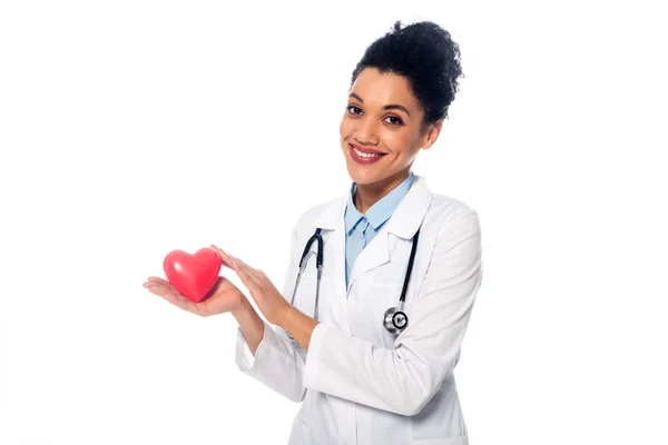 Medico afroamericano con stetoscopio sorridente e mostrando decorativo cuore rosso isolato su bianco — Foto stock