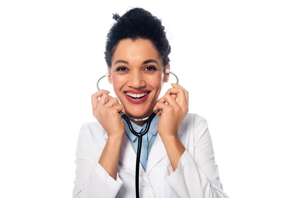 Sonriente y feliz médico afroamericano con estetoscopio mirando a la cámara aislada en blanco - foto de stock