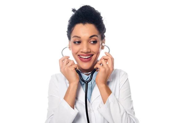 Lächelnder und positiver afrikanisch-amerikanischer Arzt mit Stethoskop, der isoliert auf weißem Grund wegschaut — Stockfoto