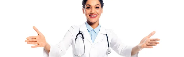 Африканский американский врач со стетоскопом и открытыми объятьями улыбается изолированно на белом, панорамном снимке — стоковое фото