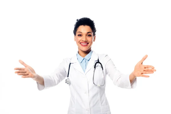 Médico afroamericano con estetoscopio y brazos abiertos sonriendo aislado en blanco - foto de stock