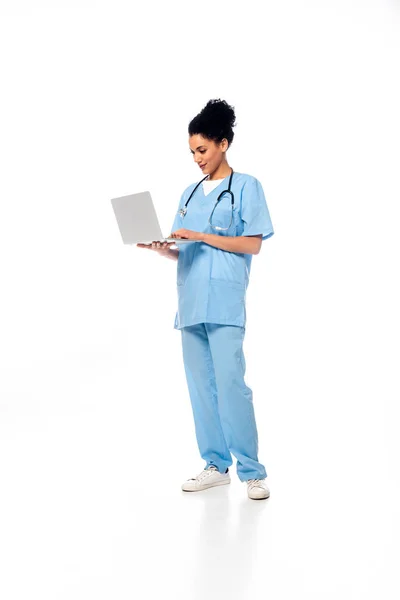 Visão completa da enfermeira afro-americana com estetoscópio usando laptop em fundo branco — Fotografia de Stock