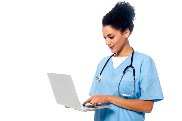 African american nurse with stethoscope focused on using laptop isolated on white — Stock Photo
