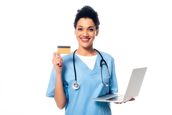 Африканская американская медсестра со стетоскопом держит ноутбук и показывает кредитную карту изолированы на белом — стоковое фото