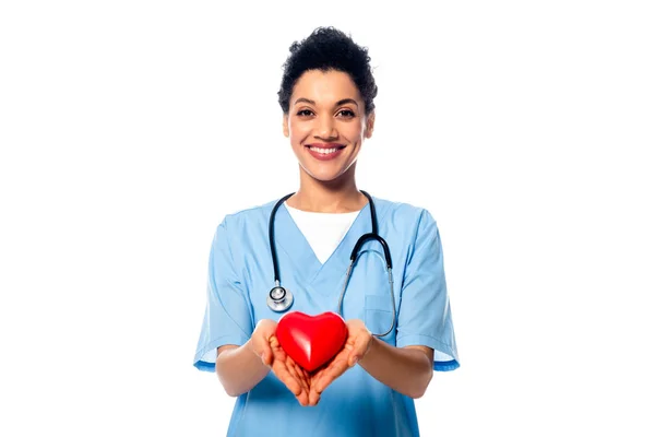 Vista frontal de enfermera afroamericana con estetoscopio mostrando corazón decorativo y sonrisa aislada en blanco - foto de stock