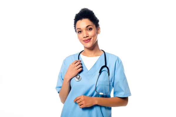 Vista frontal de enfermera afroamericana con estetoscopio sonriendo y mirando la cámara aislada en blanco - foto de stock