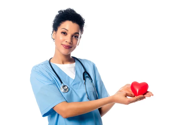 Enfermera afroamericana con estetoscopio que muestra un corazón rojo decorativo mirando a la cámara aislada en blanco - foto de stock