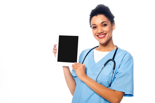 Enfermera afroamericana mirando a la cámara, sonriendo y mostrando tableta digital aislada en blanco - foto de stock