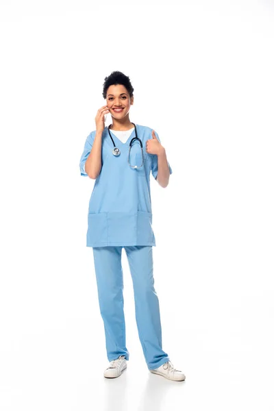 Full length view of happy african american nurse with thumb up, stethoscope and smartphone on white — Stock Photo