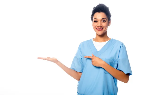 Enfermera afroamericana sonriendo y señalando con la mano y el dedo aislados en blanco - foto de stock