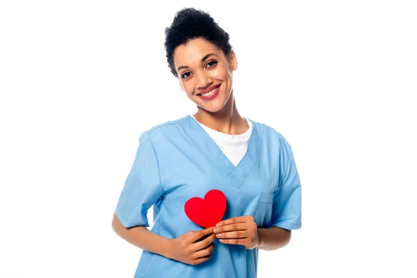 Счастливая и позитивная африканская медсестра, представляющая декоративное сердце, изолированное на белом — стоковое фото