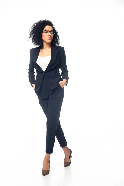 In voller Länge Ansicht der selbstbewussten afrikanisch-amerikanischen Geschäftsfrau zu Fuß mit den Händen in den Taschen auf weißem Hintergrund — Stockfoto