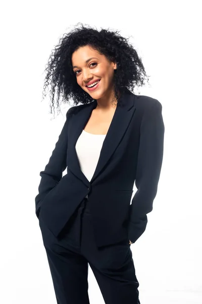 Vista frontal de la mujer de negocios afroamericana con las manos en los bolsillos sonriendo y mirando a la cámara aislada en blanco - foto de stock