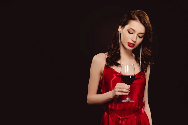 Elegante mujer en vestido rojo sosteniendo copa de vino aislado en negro - foto de stock