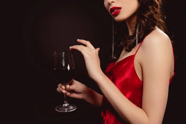 Vista ritagliata di elegante giovane donna che tiene un bicchiere di vino rosso isolato su nero — Foto stock