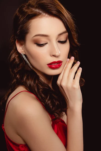 Vue latérale d'une jolie femme brune aux lèvres rouges et à la main près du visage isolée sur noire — Photo de stock