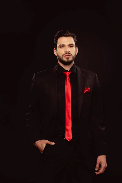 Schöner Mann im Anzug und roter Krawatte mit Blick auf Kamera isoliert auf schwarz — Stockfoto