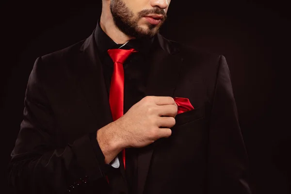 Vista recortada de hombre elegante en traje ajustando pañuelo aislado en negro - foto de stock