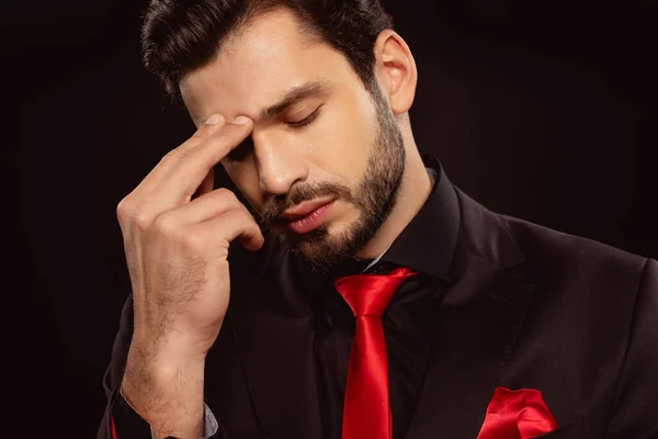 Homme pensif en costume et cravate rouge avec les doigts près du front isolé sur noir — Photo de stock
