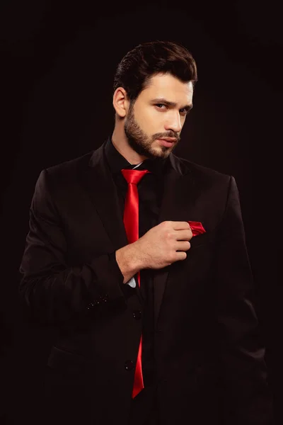 Elegant man in formal wear adjusting handkerchief and looking at camera isolated on black — Stock Photo