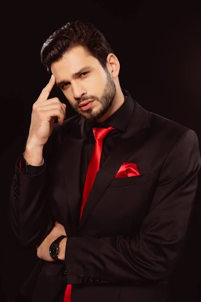 Hombre guapo en traje y corbata roja mirando a la cámara aislada en negro - foto de stock