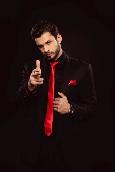 Handsome man in suit pointing with fingers and looking at camera isolated on black — Stock Photo