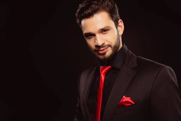 Handsome man in formal wear and red tie looking at camera isolated on black — Stock Photo